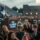 A photo of a graduation ceremony crowd, booing and heckling a guest speaker pushing AI. The speaker is a humanoid robot.